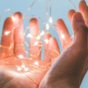 Mains tenant des petites lumières LED scintillantes, symbolisant les économies d'énergie et les conseils du guide 2025 pour réduire sa facture d'électricité
