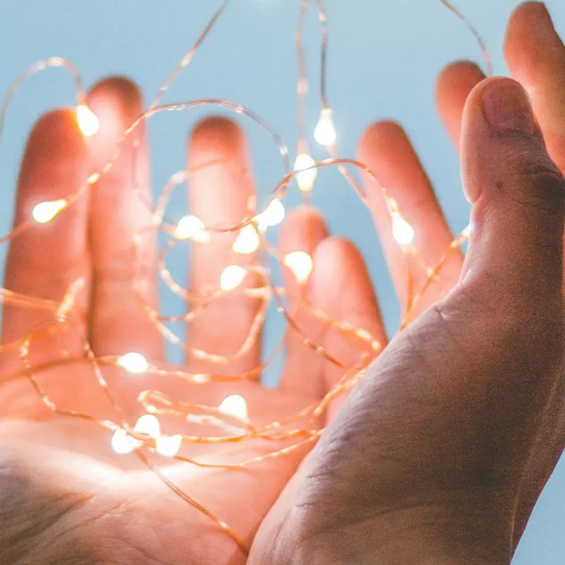 Mains tenant des petites lumières LED scintillantes, symbolisant les économies d'énergie et les conseils du guide 2025 pour réduire sa facture d'électricité
