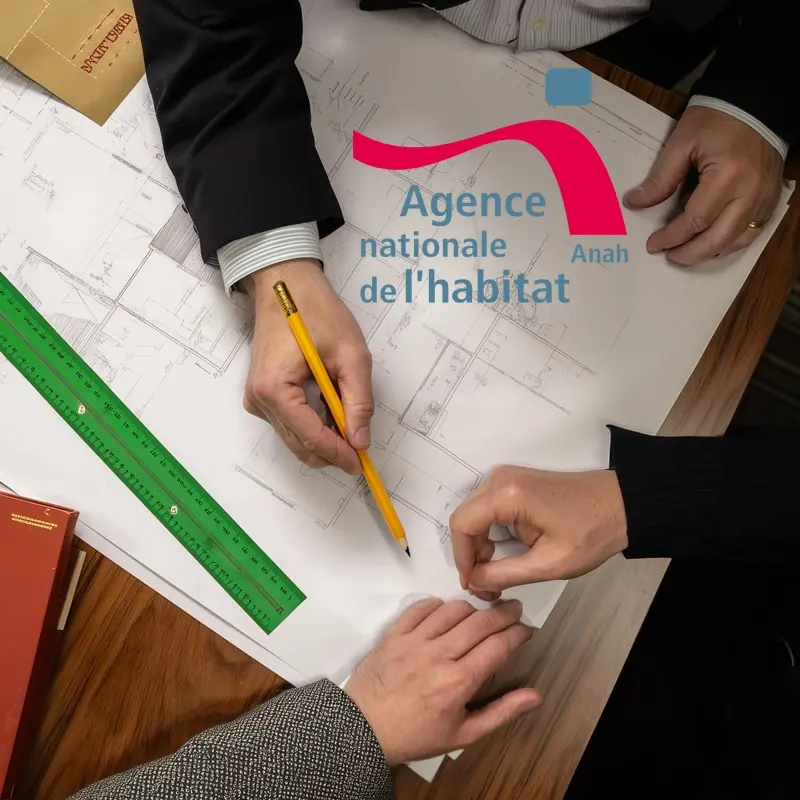 Professionnels examinant des plans avec le logo de l'Agence Nationale de l'Habitat (Anah), illustrant les travaux de rénovation éligibles aux aides Anah
